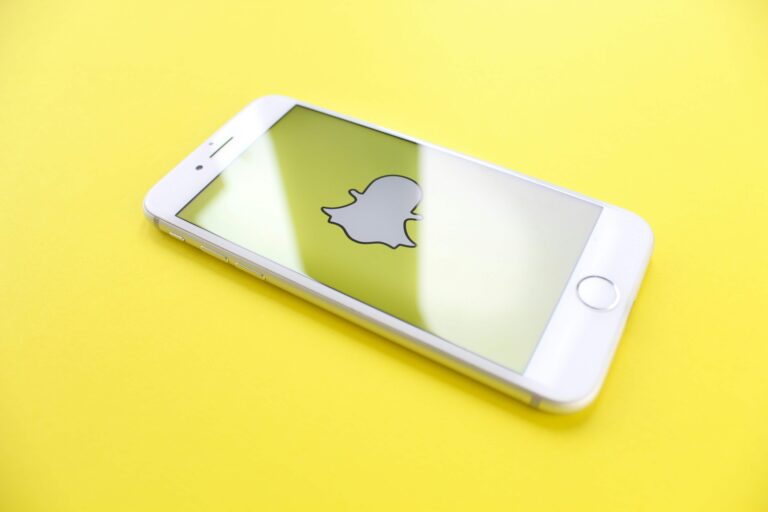 An image of a snapchat logo on a phone with a yellow background.