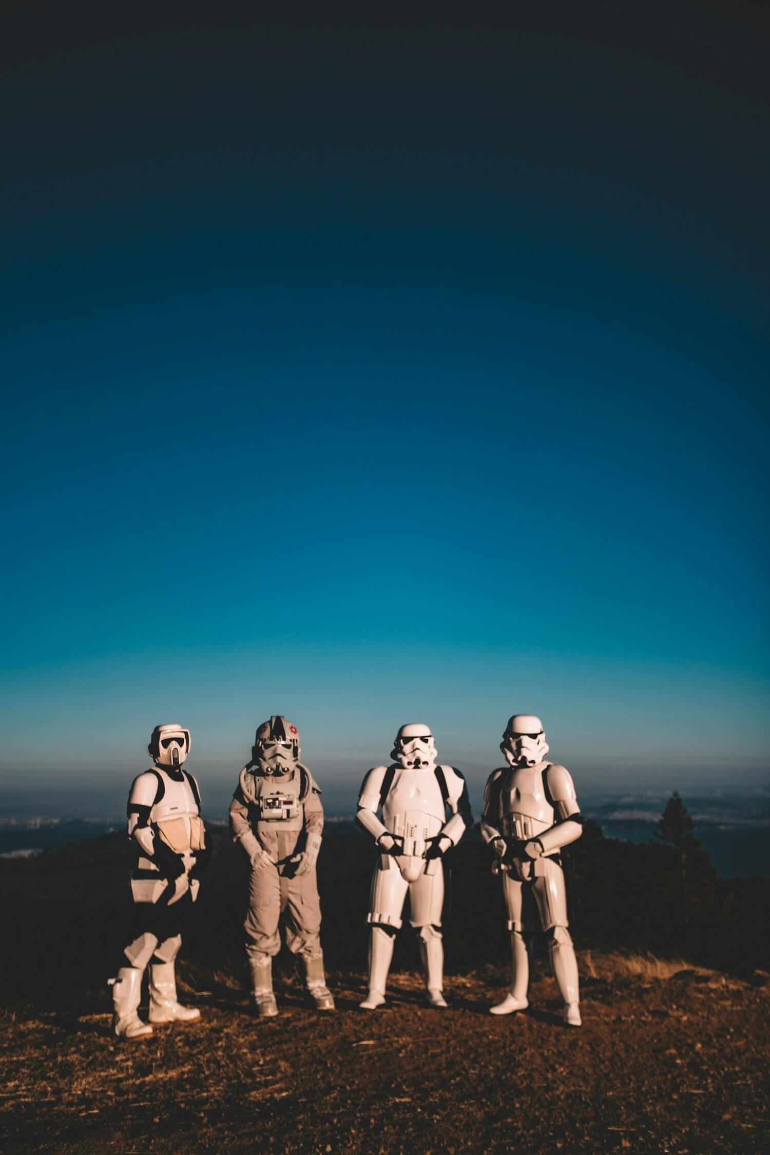 A picture of four storm troopers from start wars standing on a hill with a blue sky behind them.