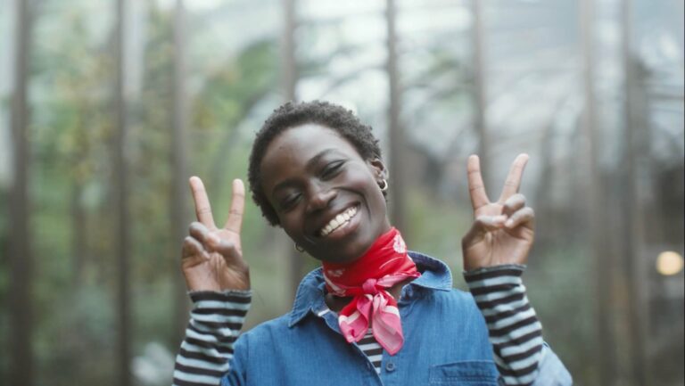 A picture of a FatFace model with a red handkerchief around her neck smiling with two piece signs to camera.