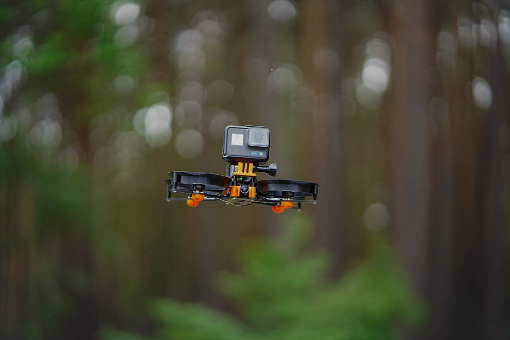 An image of an FPV drone with a GoPro on infront of a woodland.