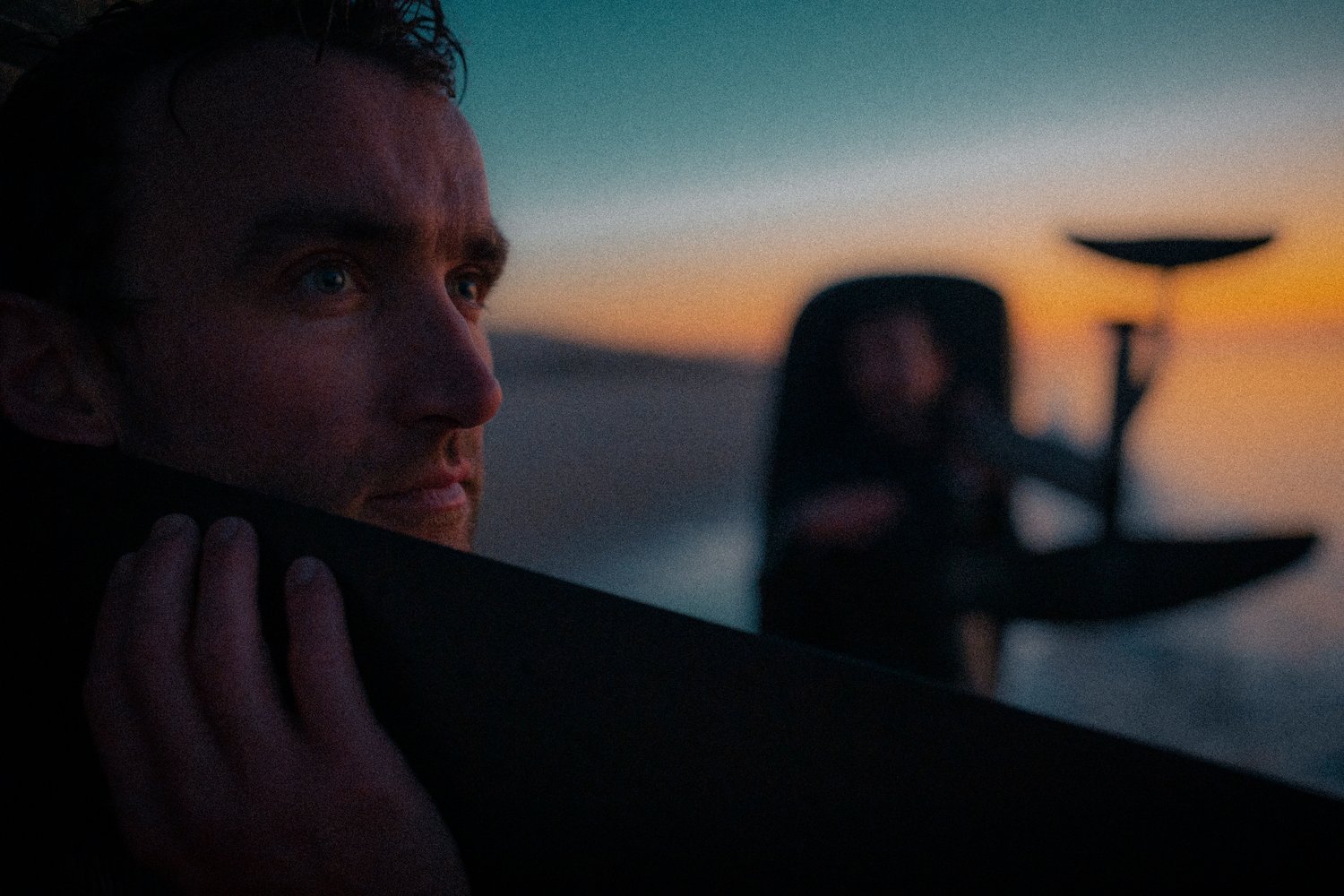 An image of Hugo Turner looking out over a sunset holding a Flite Board over his shoulder.