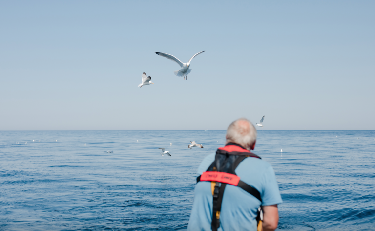 A still frame from our documentary with the wildlife trust showing a fishermen in yellow and blue overalls looking over a deep blue sea.