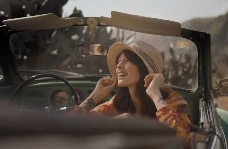 A FatFace model in the front seat of a Beetle Car parked beside a road in Tenerife, Canary Islands.