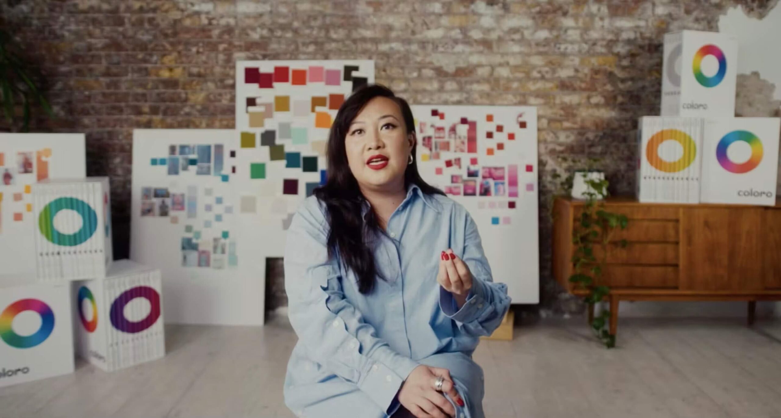 An image of a lady on a chair in a studio with lots of colour behind her.