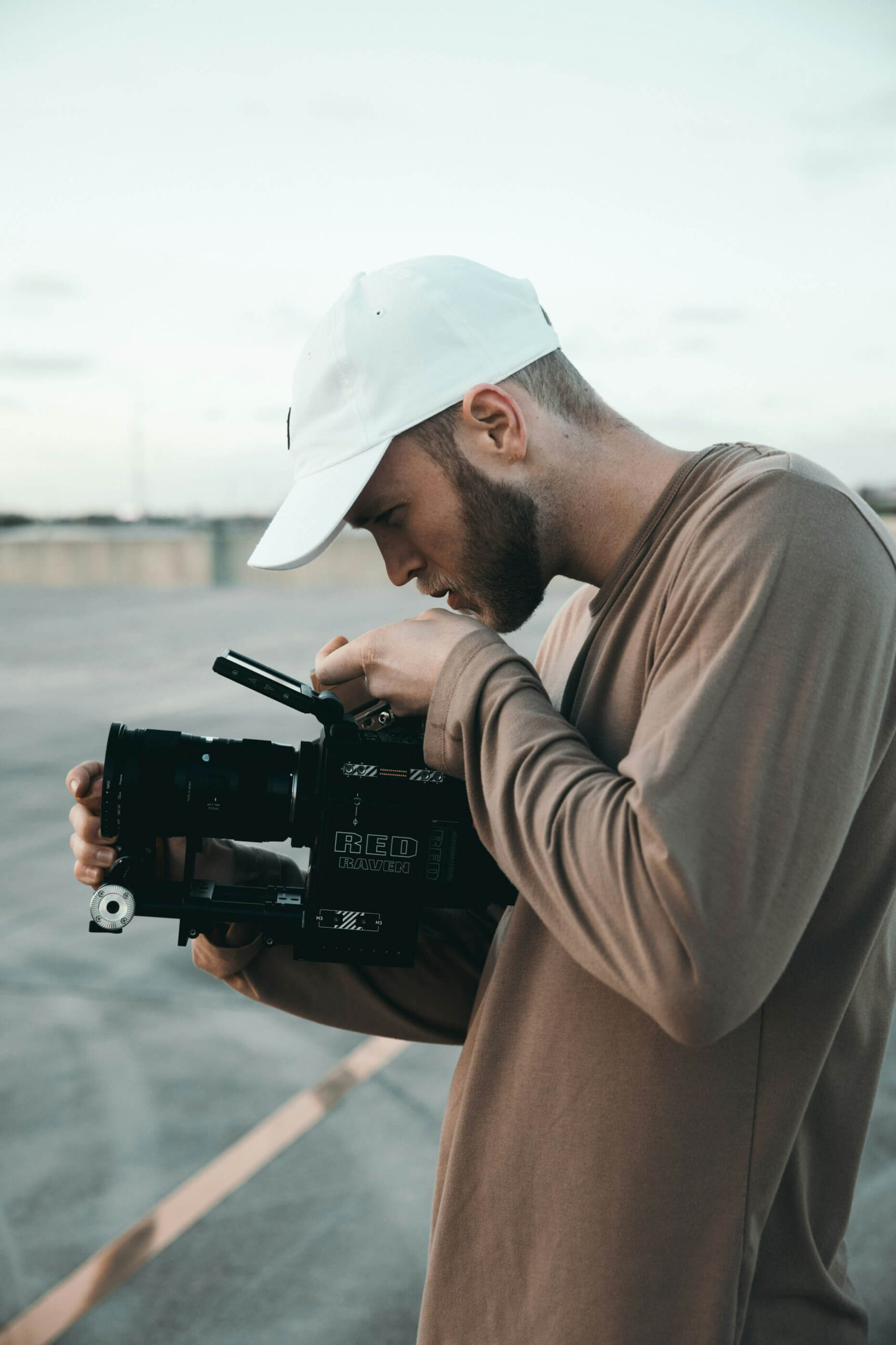 a videographer is a brown crew jumper, with a white hat and a camera.