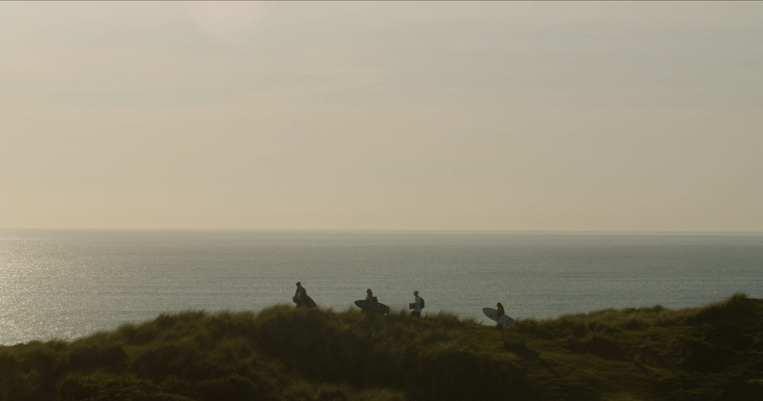 An image of four people walking over a sand dune at Godrevy with the sea and sun in the background.