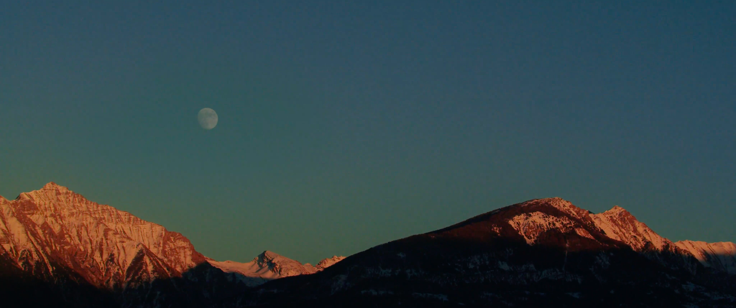 Snow capped alps in the evening with a full moon in a dark blue sky.