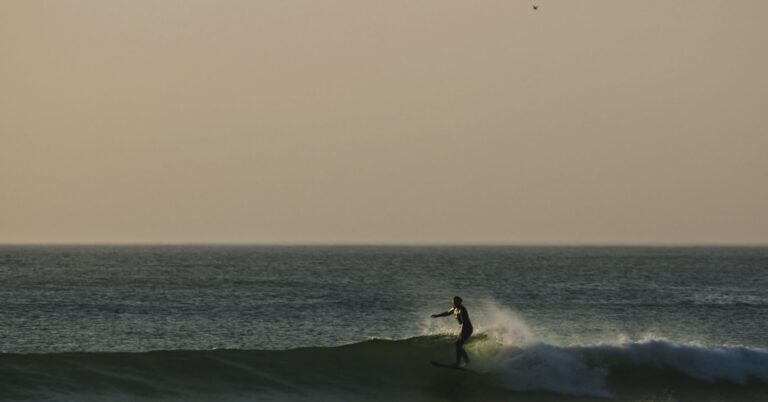 An Image of Tassy Swallow surfing a wave with the sun setting behind her.