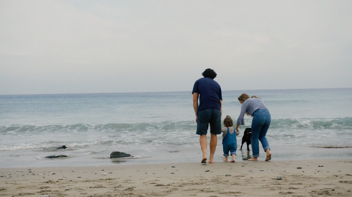 An image of Jackson and Carly, a local family in Cornwall, walking on their local beach with their child Noa.