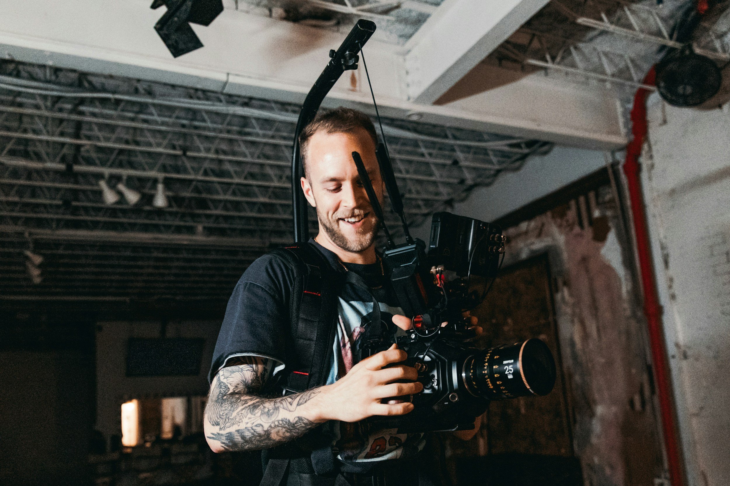 A director of photography (DOP) with an easy rig back pack on a film set. He is smiling holding a camera.