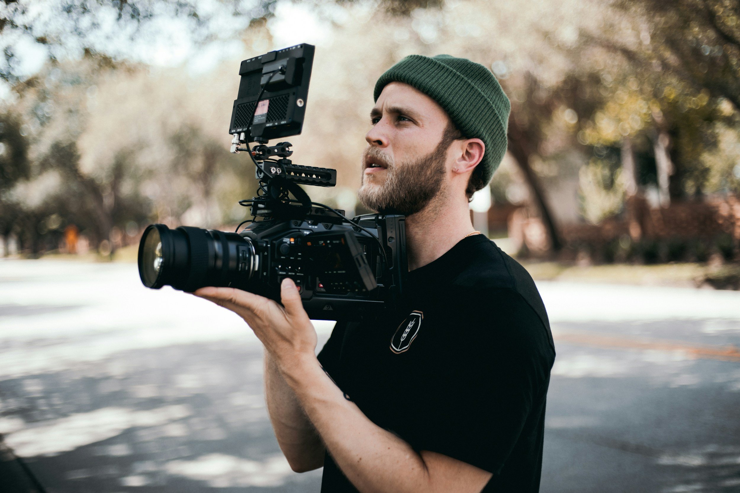 A videographer with a black tshirt and a beanie hat on holding a camera.