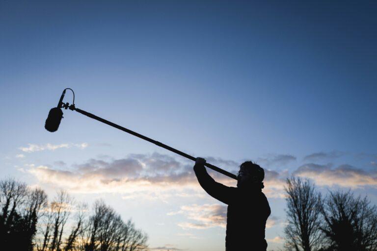 An image of a sound man holding a boom pole with a blue sky behind him.