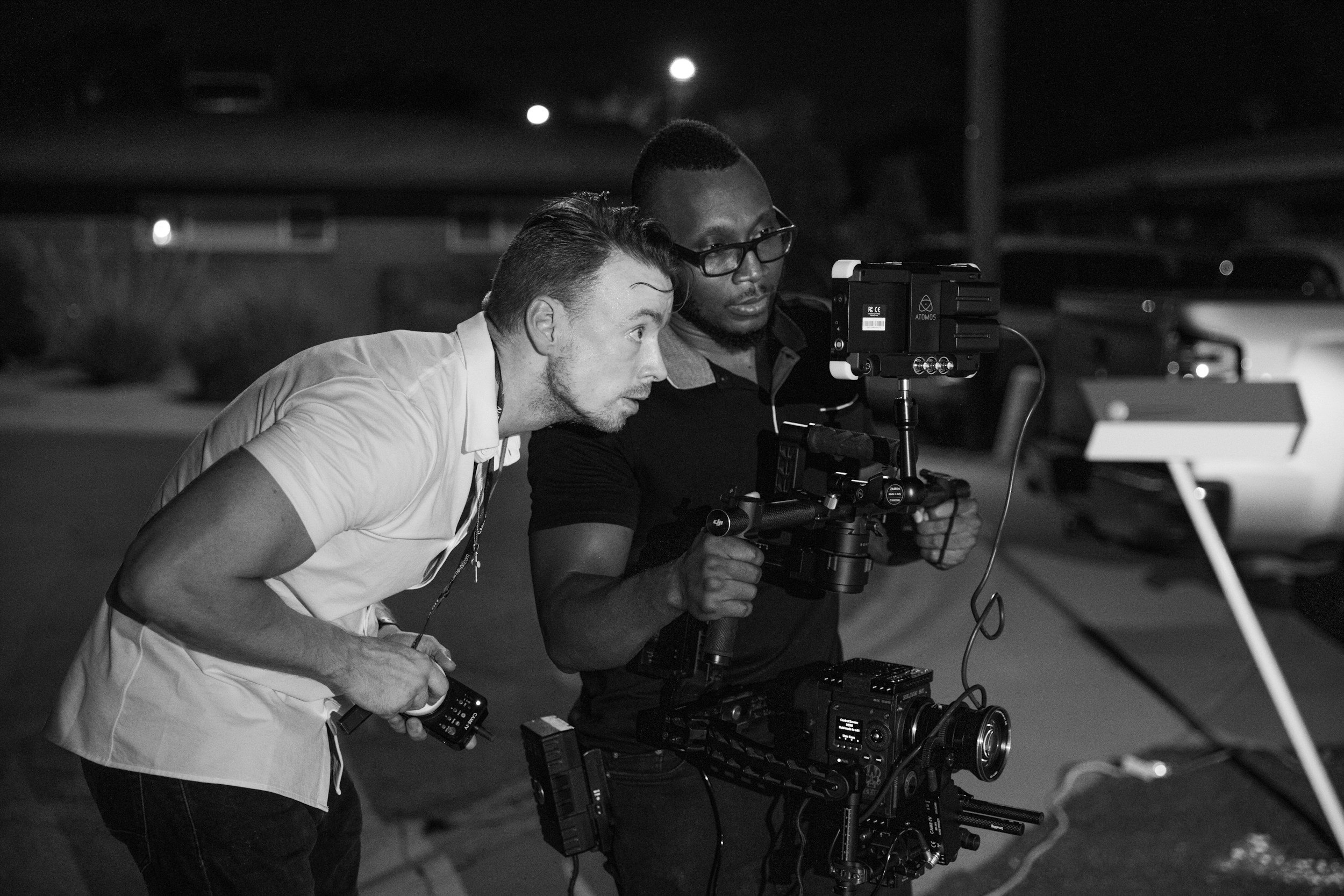 a black and white image of a film director and an assistant looking into the screen of a cinema camera