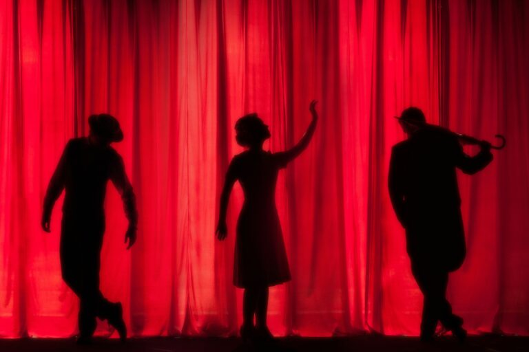 A silhouetted image of different cast members on stage behind a red curtain.