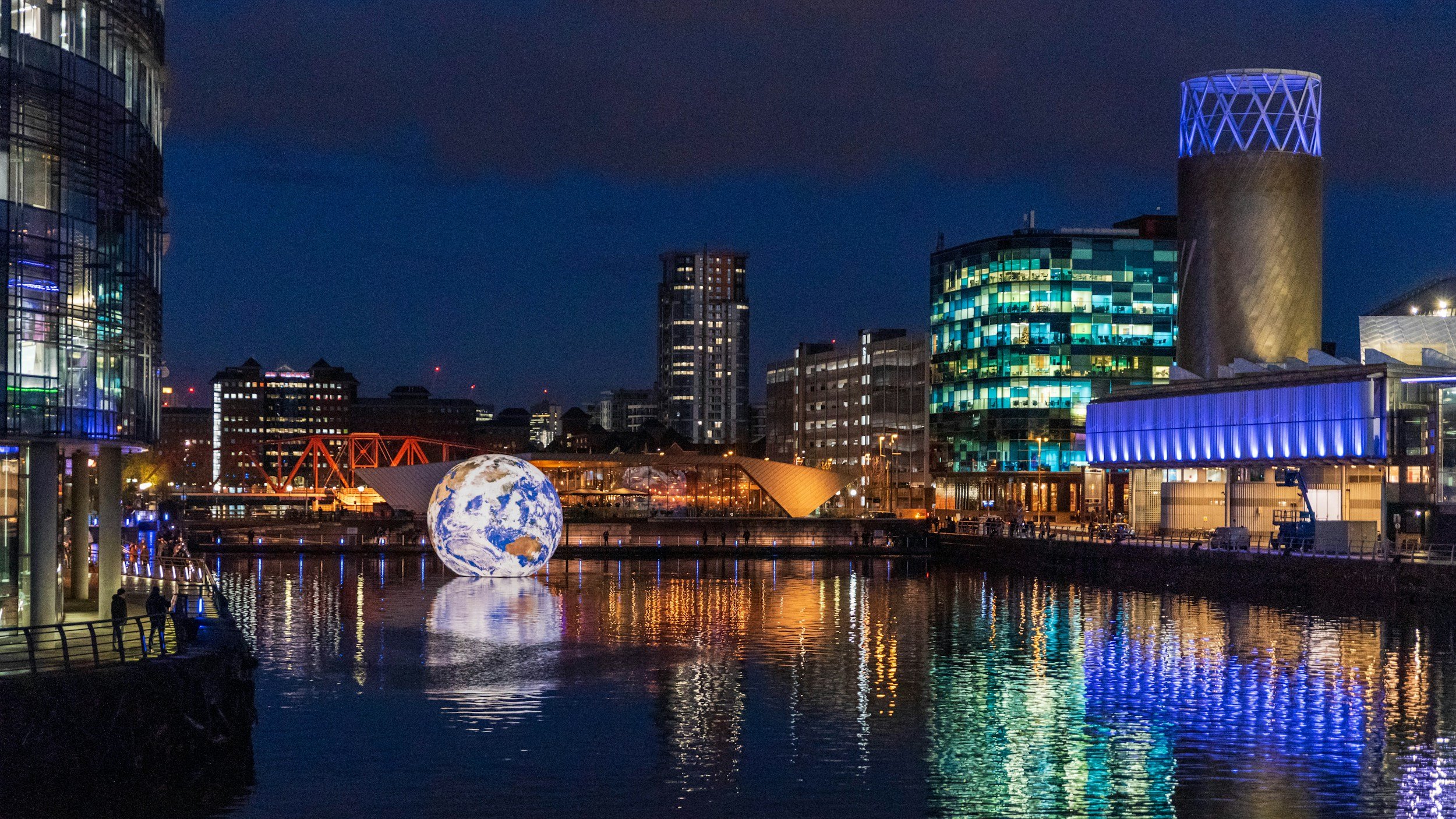 A night time shot of Salford Quays with lights streaming across the water