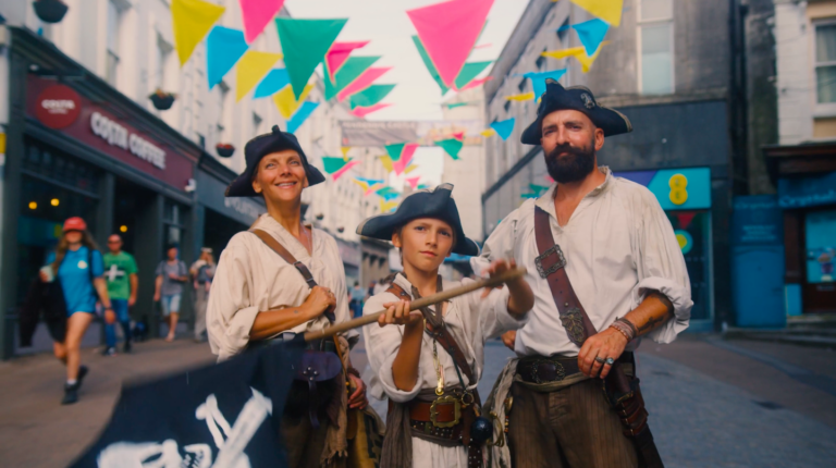 An image of a family at the Falmouth Sea Shanty Festival dressed up as pirates waving a flag.