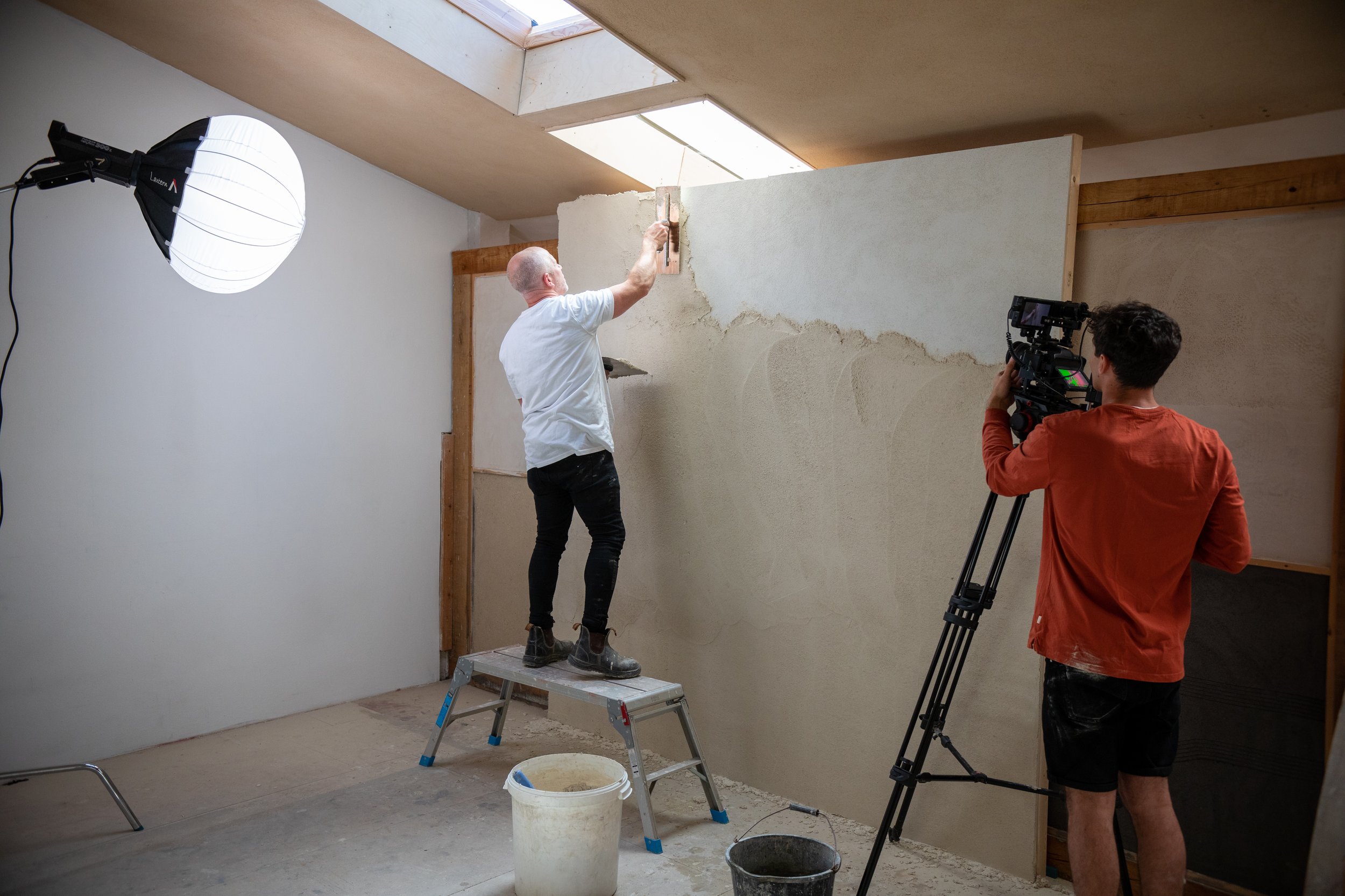 An image of a Clay Works plasterer wearing a white t shirt finishing off a wall with white plaster.