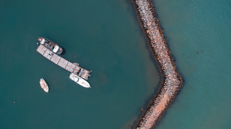 An arial shot of a harbour looking straight down. We see tankers and a blue ocean.