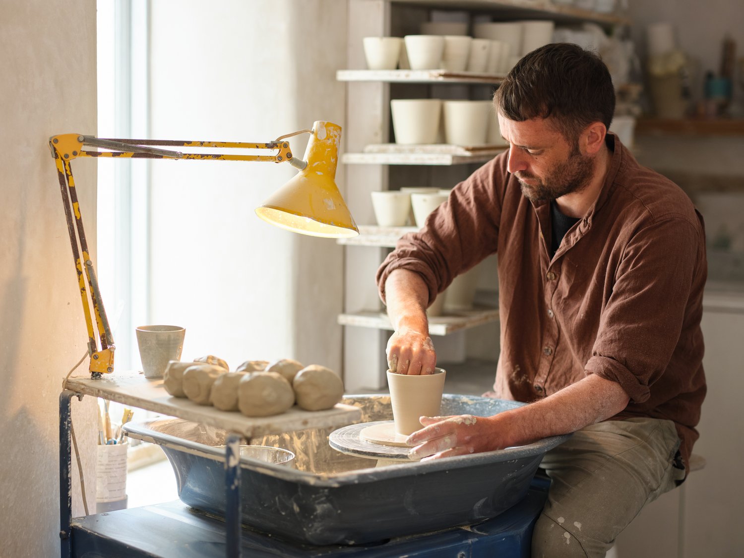 An image of Jake Boax on his potting wheel in his studio in POrthleven. He's wearing a brown shirt with a pale cream background.