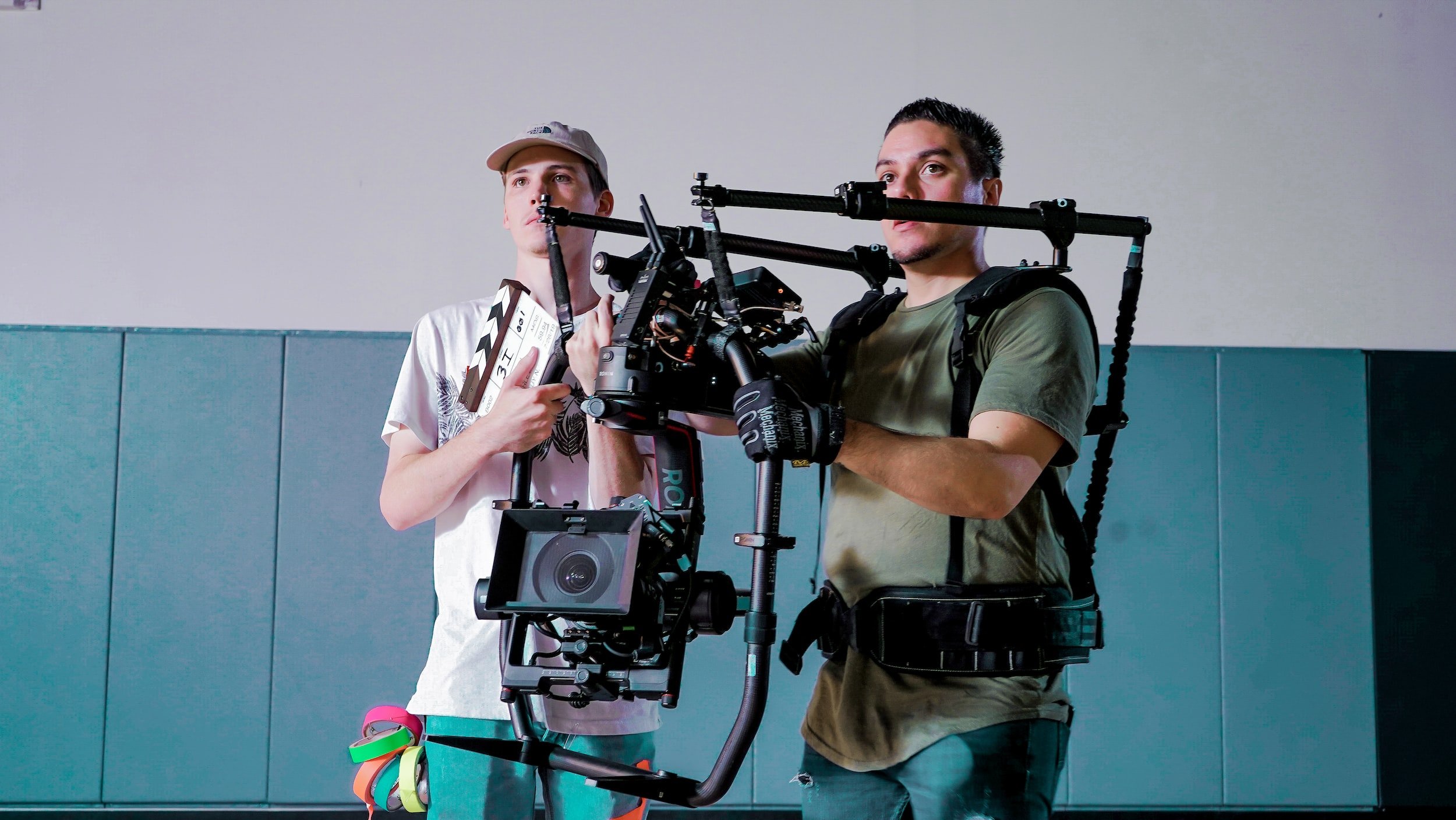 A camera man and director standing side by side. The camera man is holding a giant gimbal and camera.