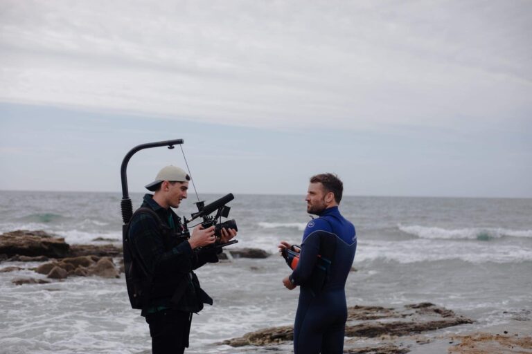 Oliver couch, creative direcvtor of Here Now Films, pointing a camera at a surfer in Cornwall before he gets in the sea.