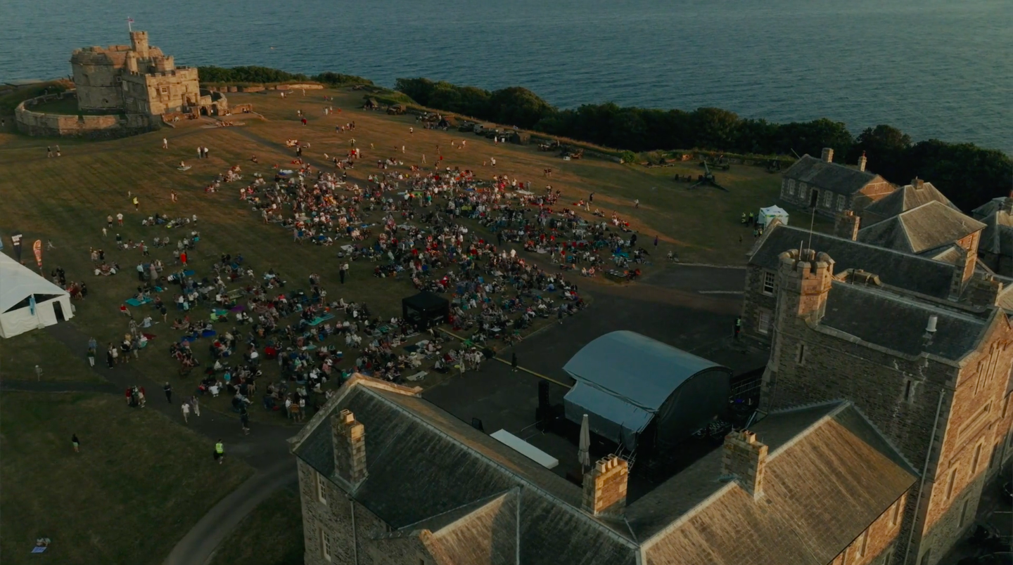 An image of Falmouth Castle in Cornwall with hundreds of people sitting on the grass waiting for a band to start playing for the National Armed forces day afterparty.