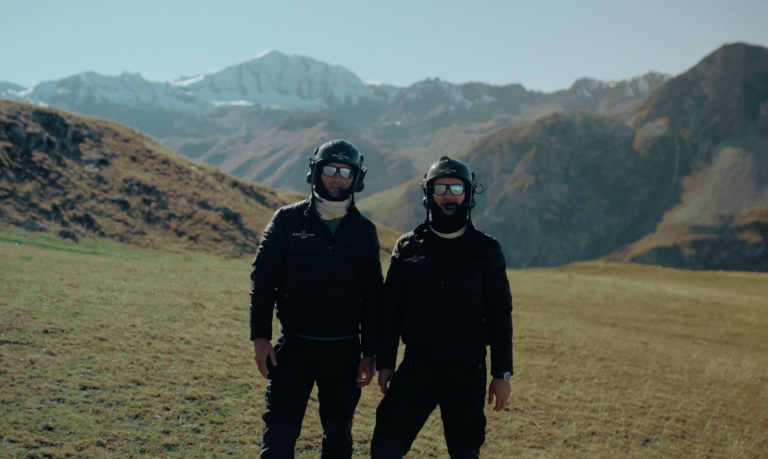 The Turner Twins standing next to each other in the alps with their flight gear on.