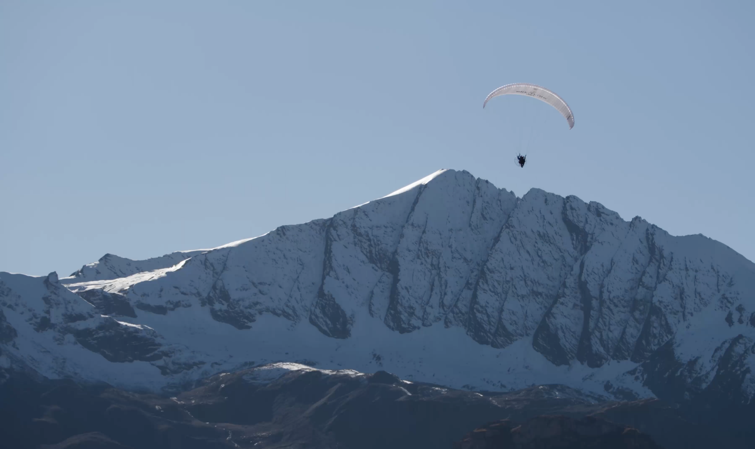 An image of the Alps mountains with a paraglider just visible over the mountain peaks.