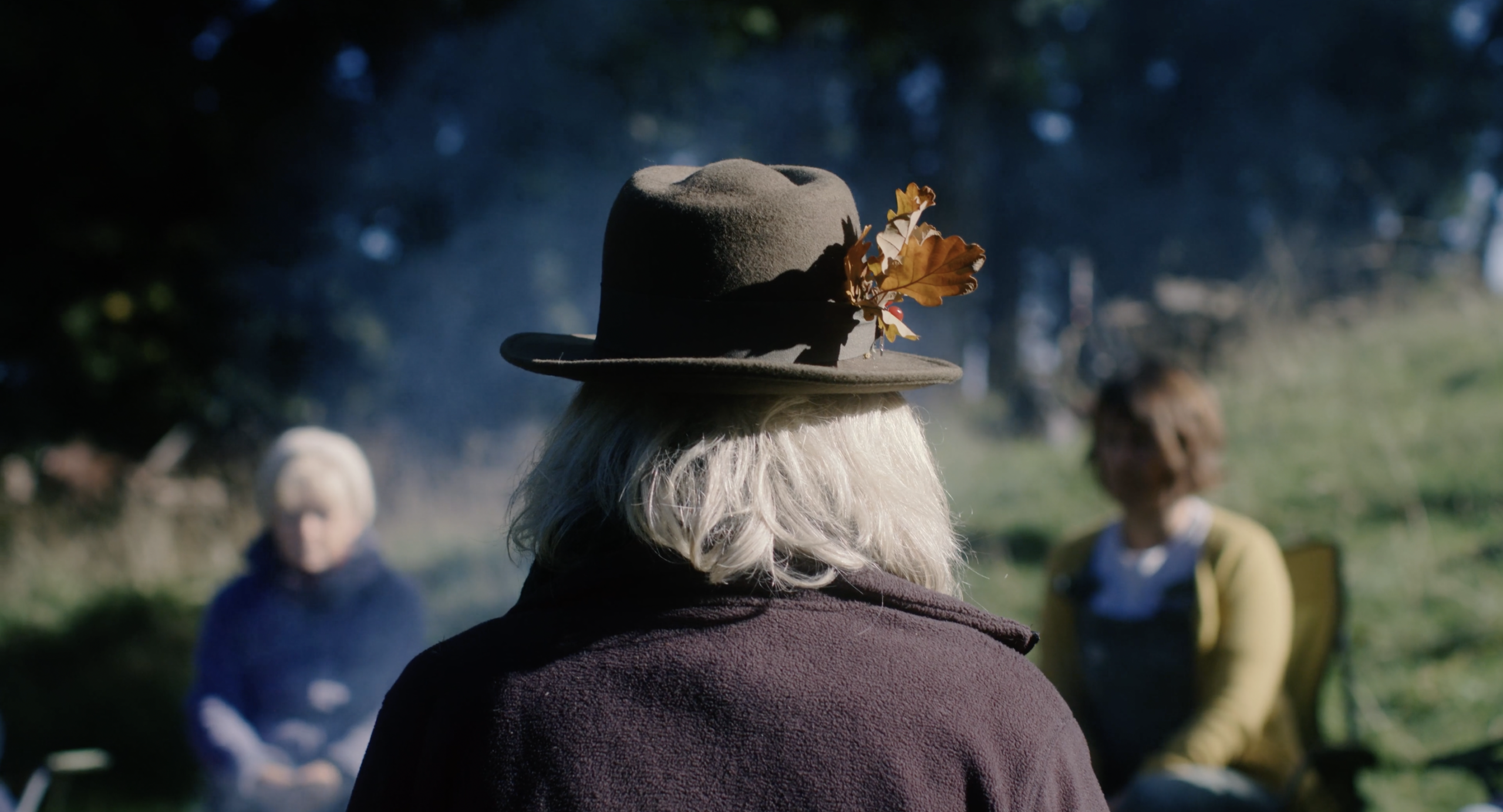 An image of the back of a woman's head wearing a hat with a feather poking out the top.